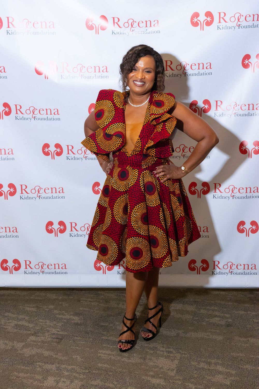 Woman in vibrant African print dress poses at Roeena Kidney Foundation event backdrop.
