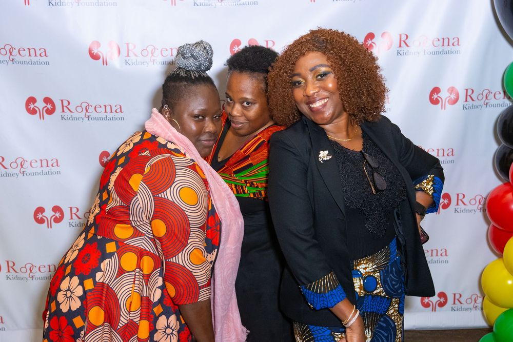 Three women posing together at a Rogena Kidney Foundation event in front of a branded step-and-repeat banner.