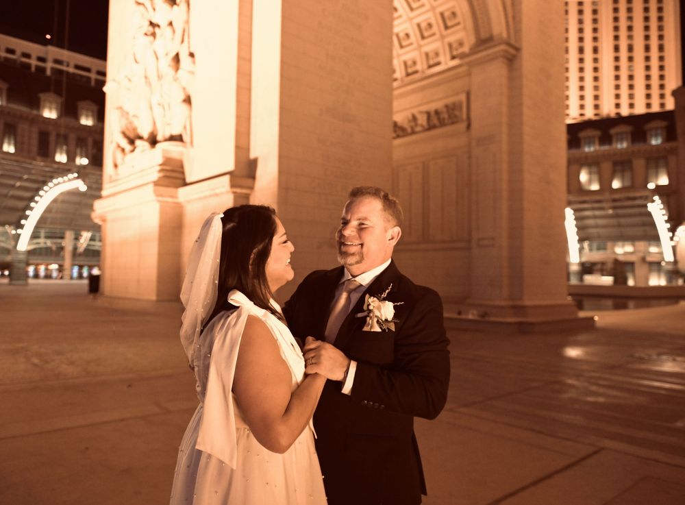 Newlywed couple sharing a romantic moment at night outside a grand columned building in Las Vegas.