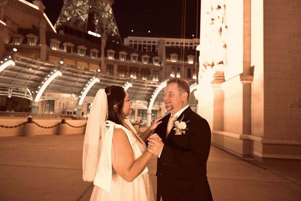 Bride and groom share a romantic moment at night with illuminated city buildings in the background.