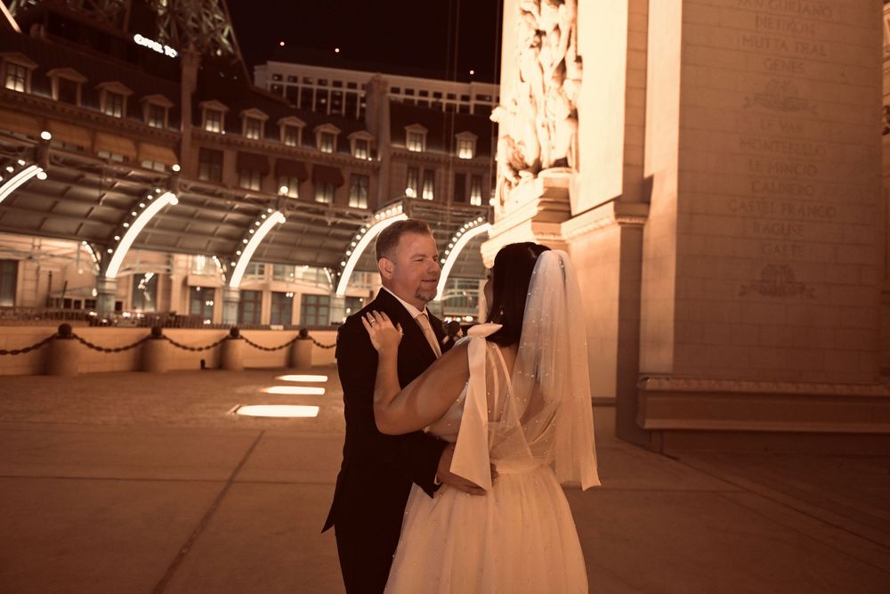 A bride and groom share a romantic dance outside an illuminated building at night during their wedding celebration.