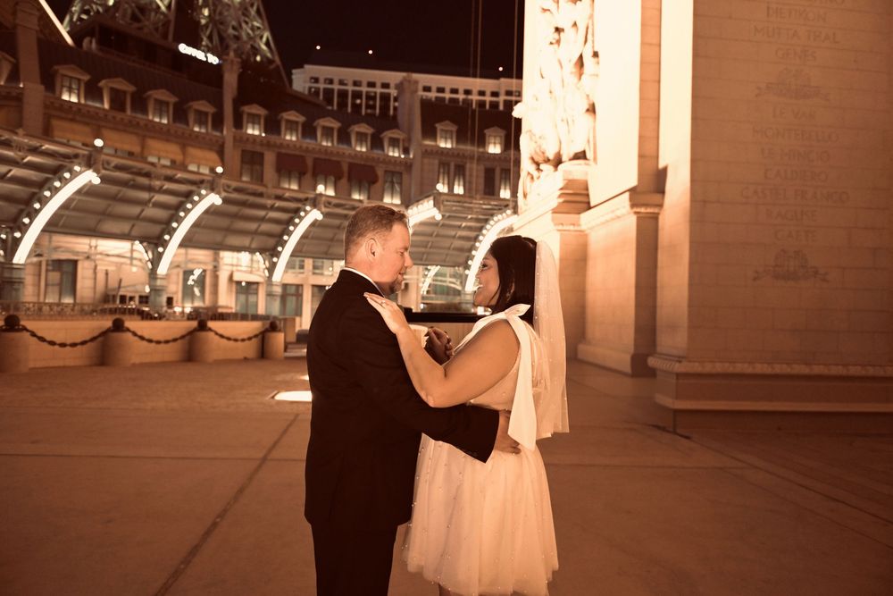 Couple sharing a romantic dance outdoors at night near illuminated classical architecture columns.