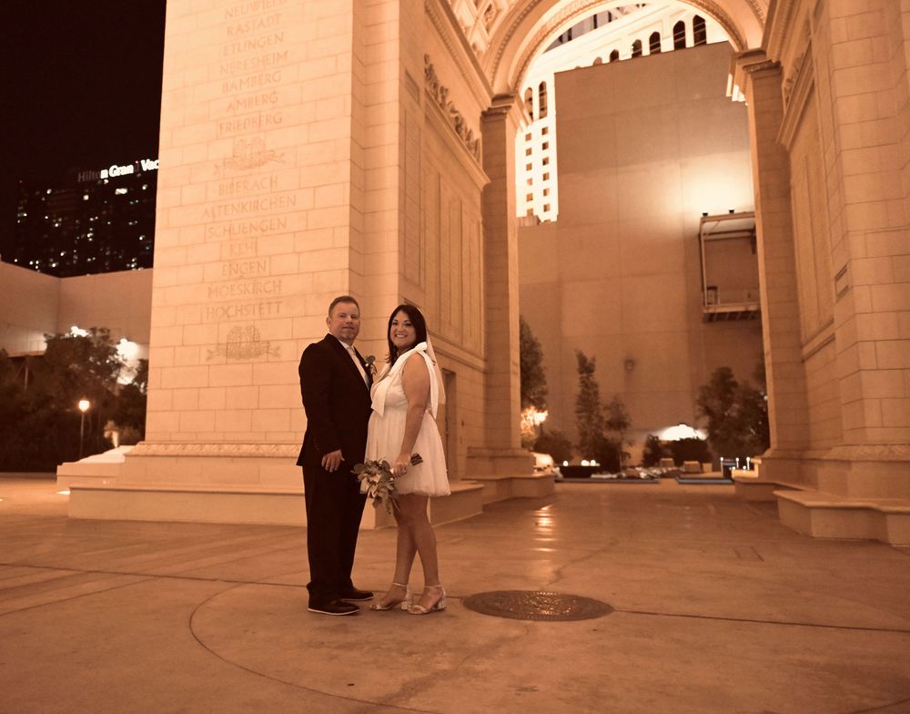 Couple poses for wedding photo at night under grand illuminated arch in Las Vegas.