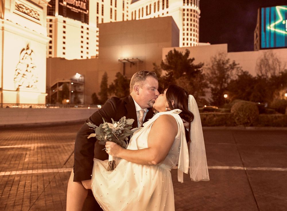 Bride and groom share a romantic kiss on the Las Vegas Strip at night, bride holding a bouquet.