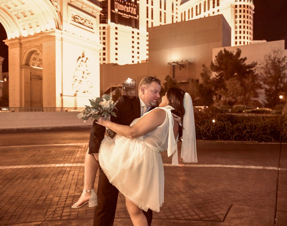 Newlywed couple sharing a romantic kiss on the Las Vegas Strip at night with casino lights glowing behind them.