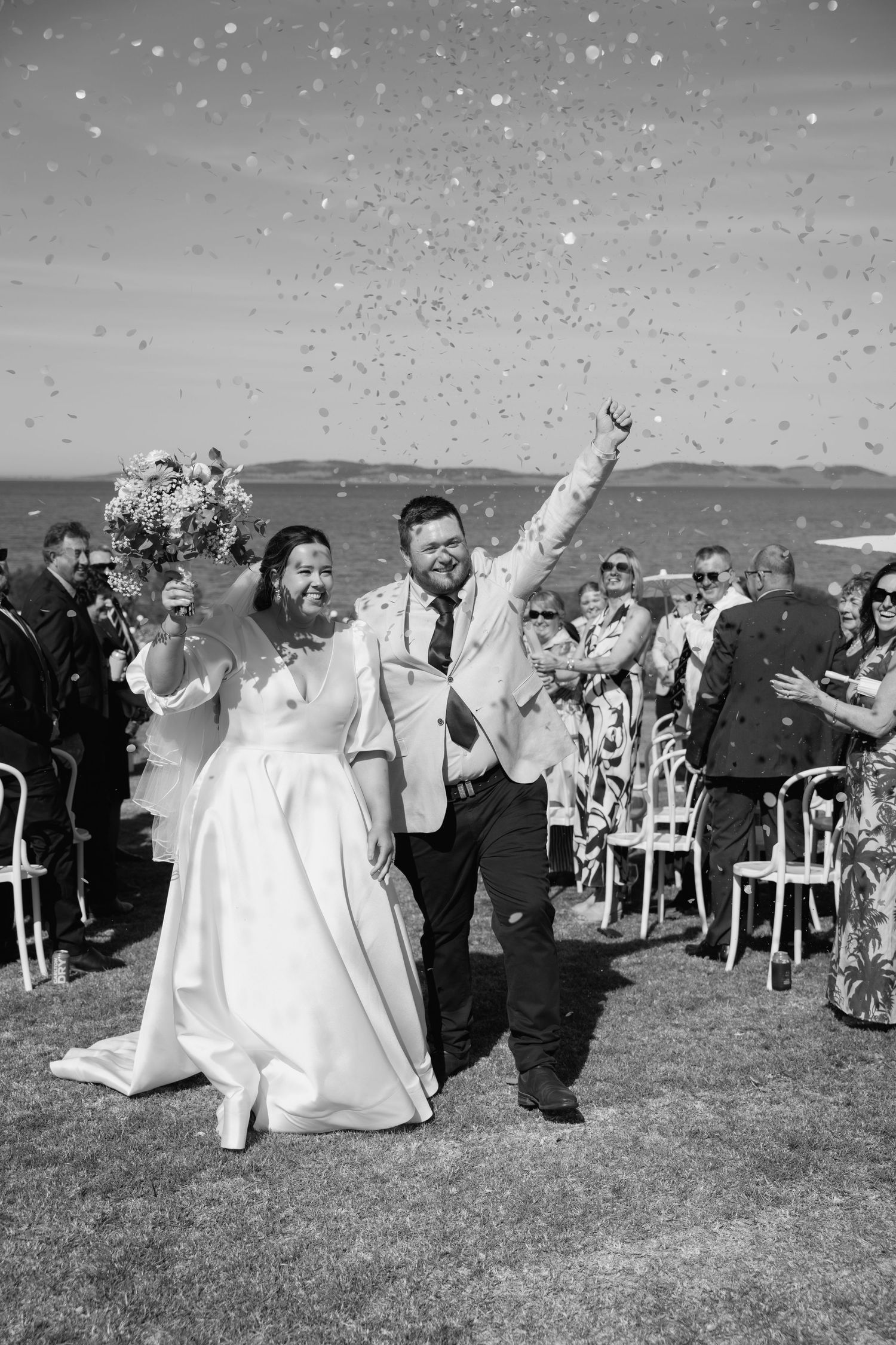 Joyful newlyweds walk down the aisle as guests throw confetti at their outdoor wedding ceremony.
