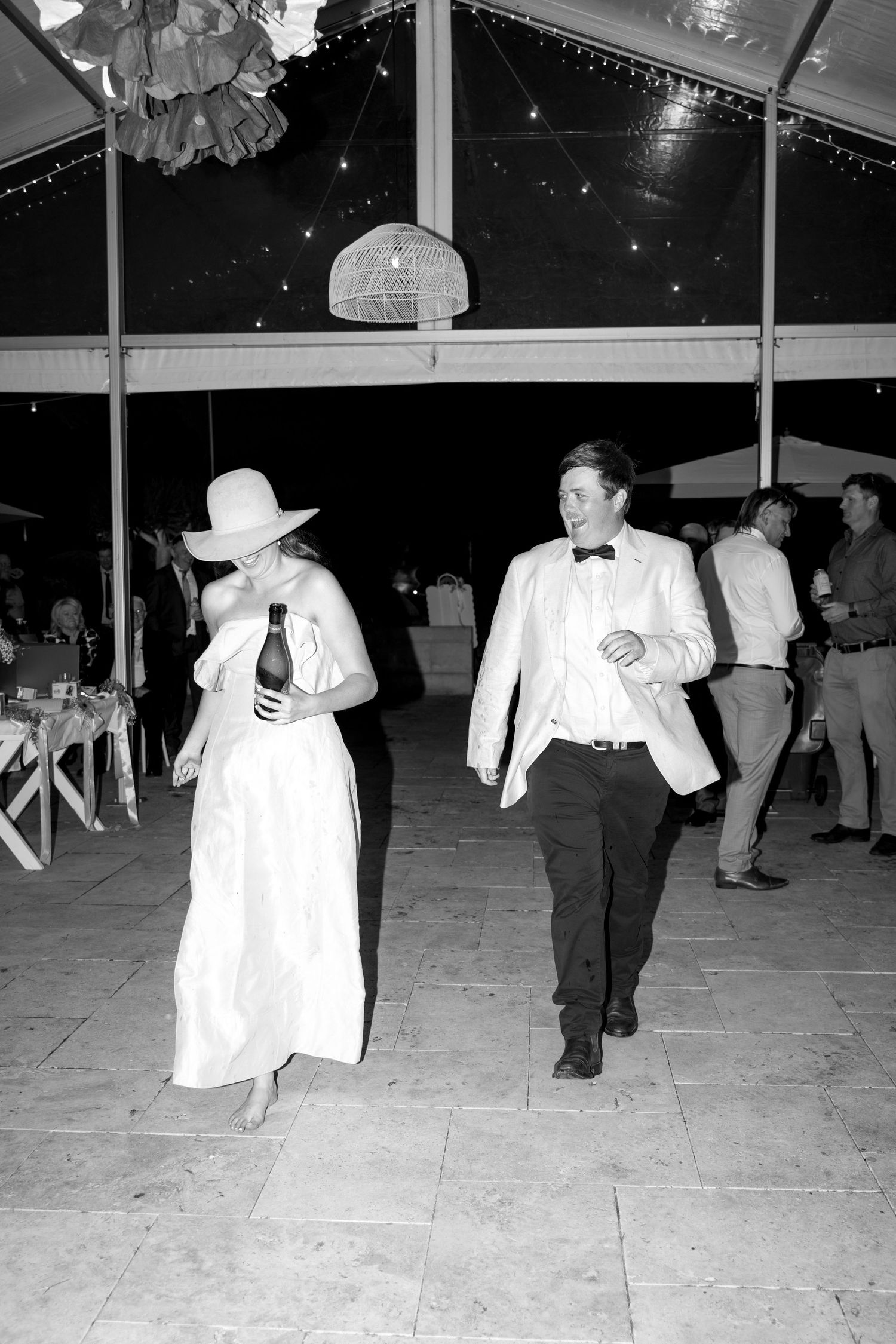 Black and white photo of a bride and groom dancing at an outdoor wedding reception under a tent at night.