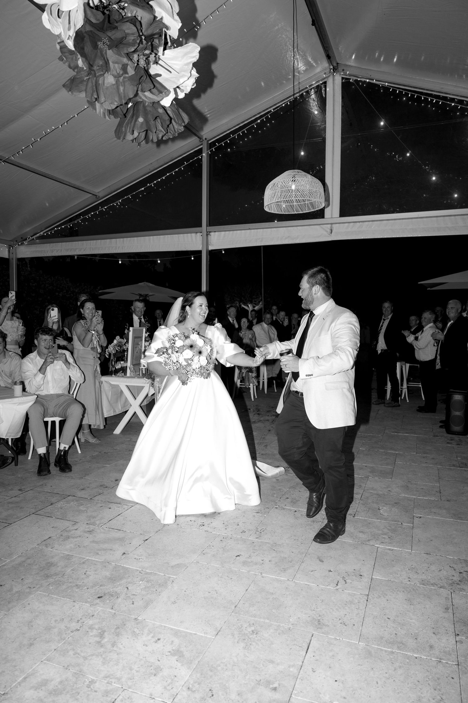 Black and white photo of bride and groom sharing their first dance under a tent at their wedding reception.