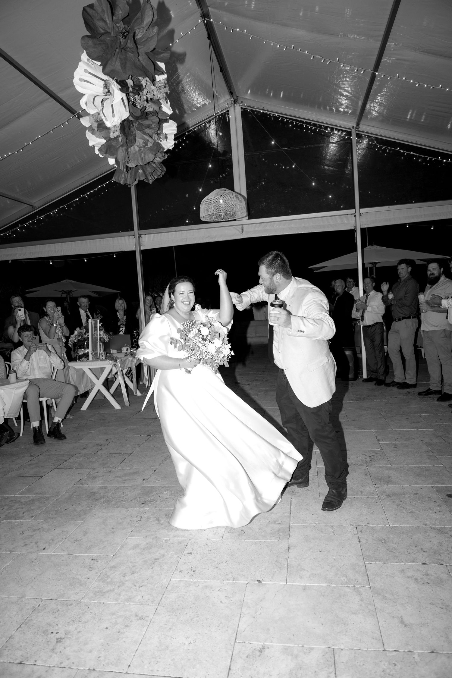 Bride and groom share their first dance under a decorated tent at their evening wedding reception.