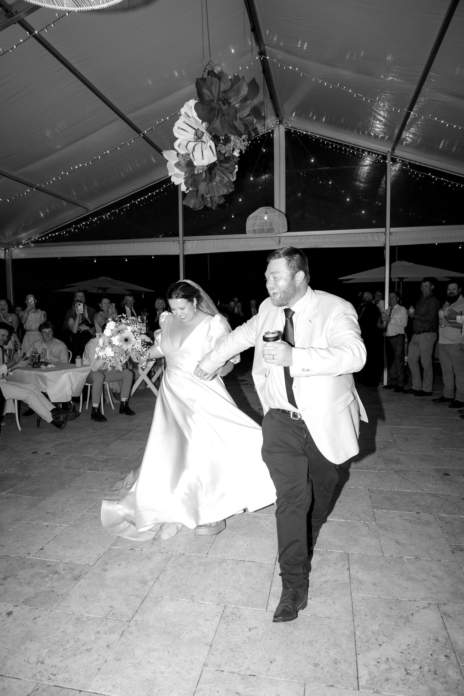 Bride and groom dance energetically together under a marquee tent at their wedding reception at night.