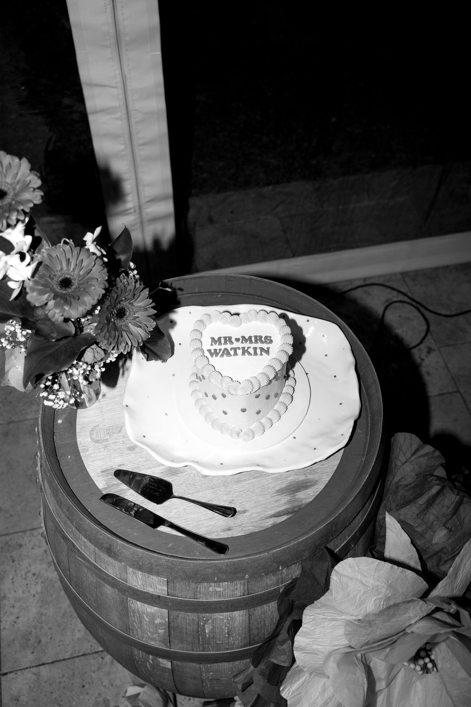 Heart-shaped wedding cake inscribed with Mr and Mrs Watkin displayed on a rustic wooden barrel.