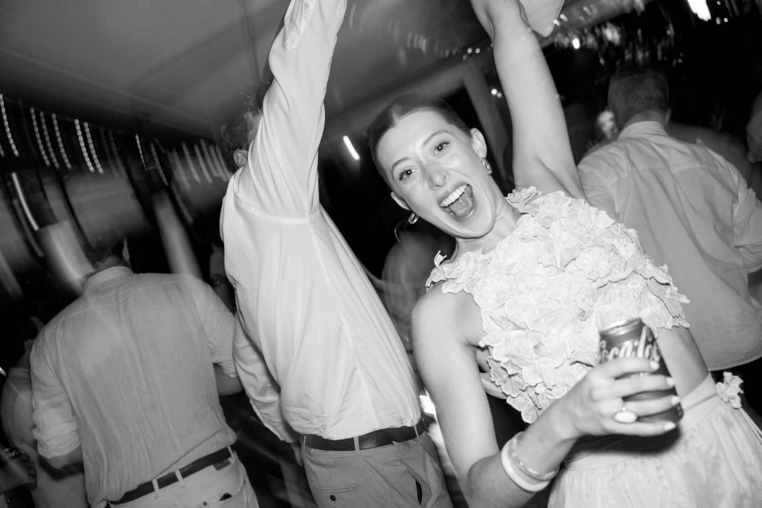 Joyful bride dancing with arms raised at wedding reception in black and white photo.