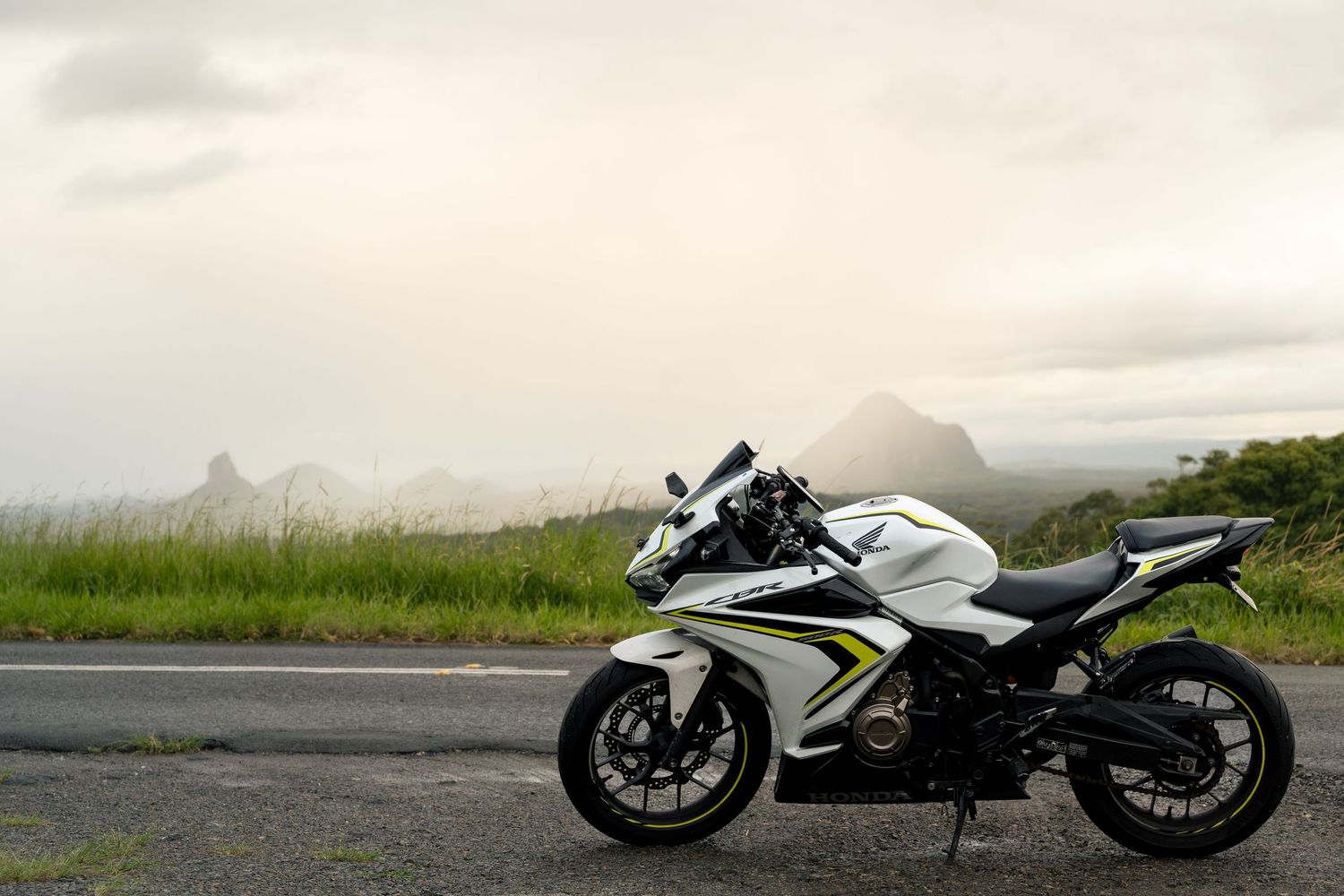White sport motorcycle parked on roadside with lush green hills and misty mountain landscape in background.