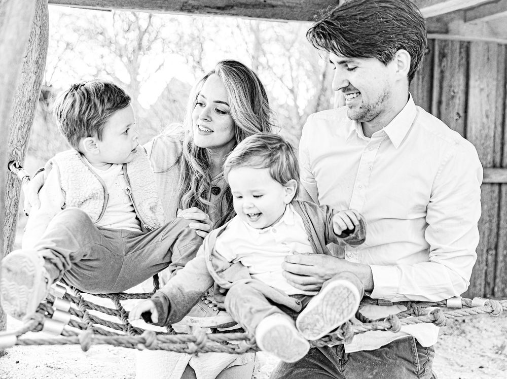 Black and white family portrait of parents with two young children laughing together in a rustic wooden setting.