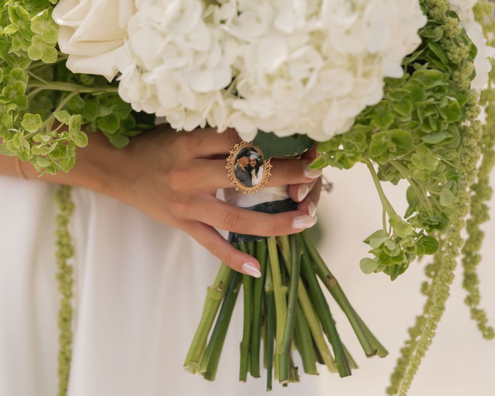 Bride holding white hydrangea wedding bouquet with green accents and gold ring on finger.
