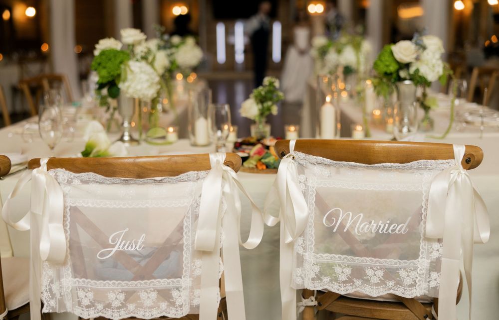 Elegant wedding reception chairs adorned with "Just Married" lace signs and white ribbon bows at a beautifully decorated venue.