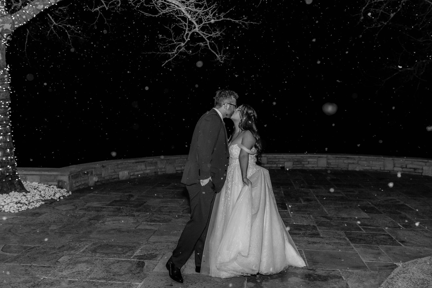 Black and white photo of a bride and groom sharing a romantic moment in the snow at night.