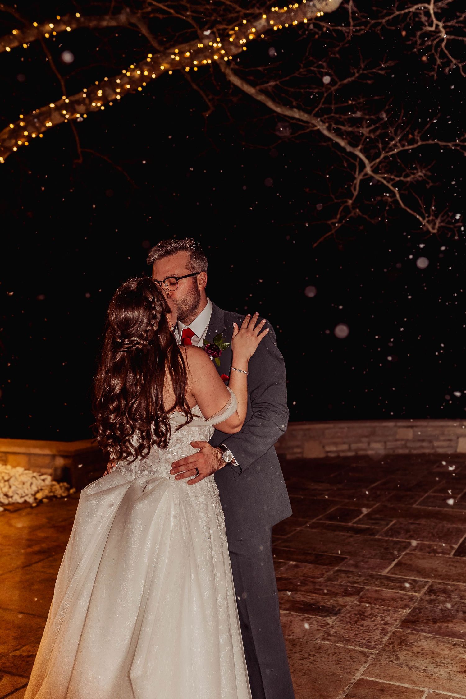 Bride and groom share romantic first dance outdoors at night, surrounded by snow and twinkling fairy lights in trees.