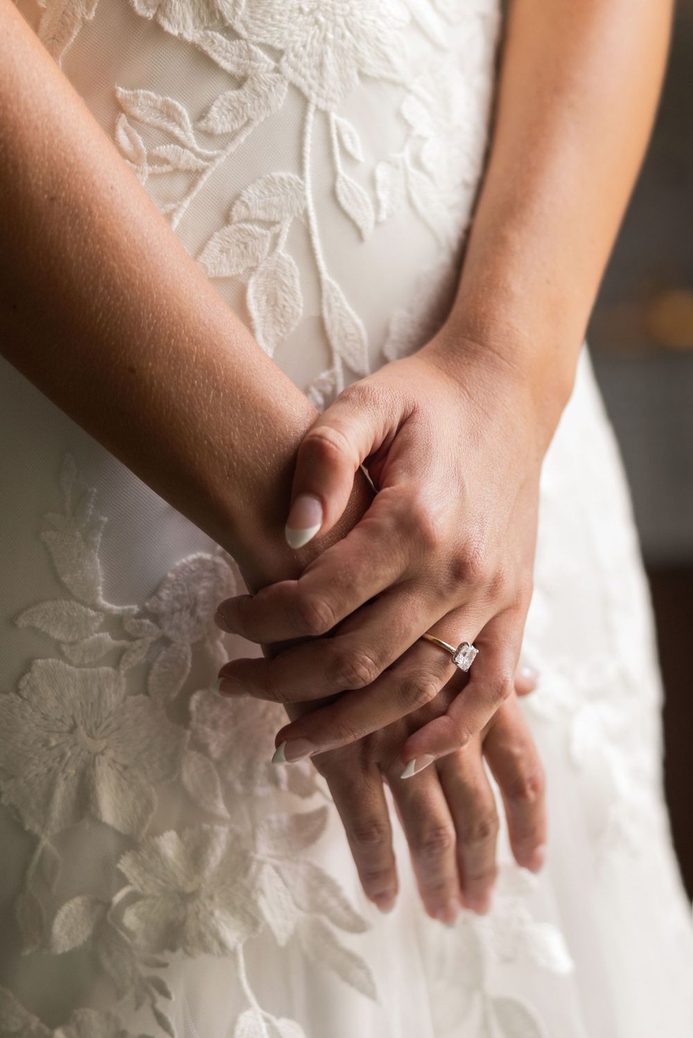 Bride in lace wedding gown clasping hands showing diamond engagement ring and wedding band.