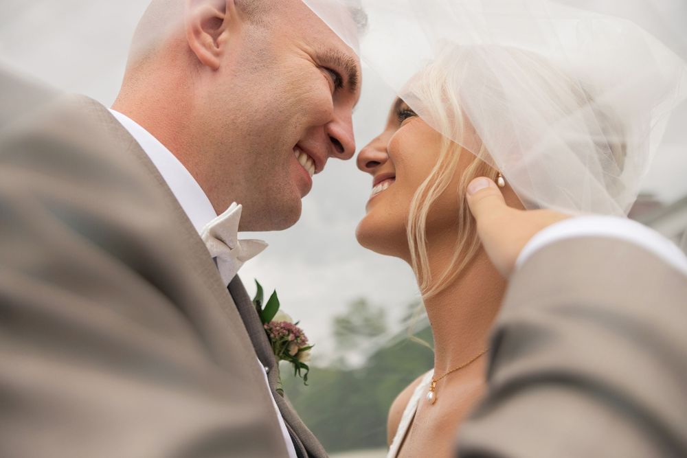A bride and groom share a romantic moment under a wedding veil, smiling at each other on their wedding day.