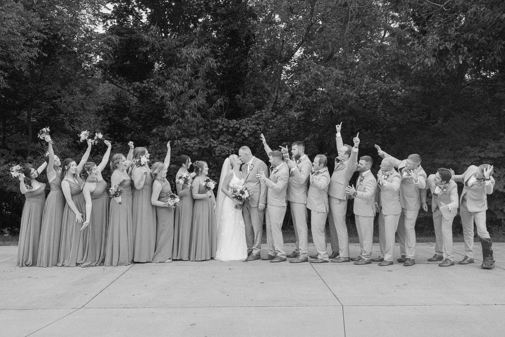 Black and white wedding party photo with bride, groom, bridesmaids, and groomsmen cheering outdoors. little brook meadows lancaster ohio.