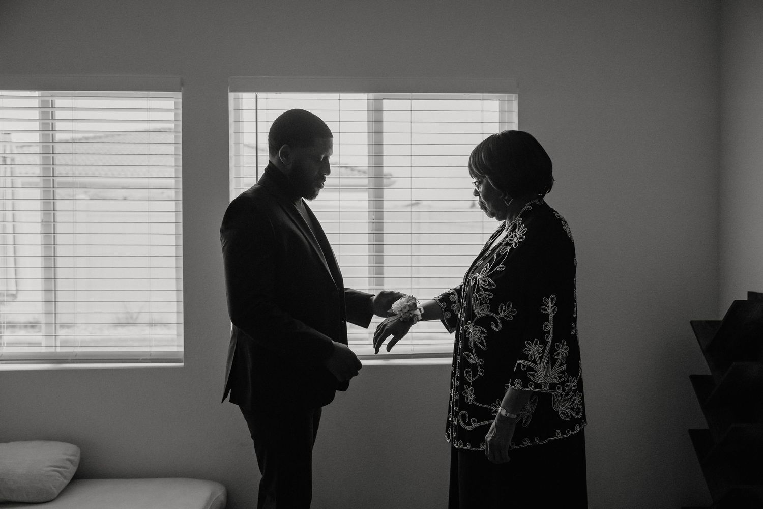 Groom being helped with cufflinks by mother in black and white silhouette photo before wedding ceremony.