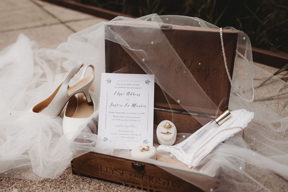 Elegant wedding flat lay with invitation, bridal heels, veil, and accessories arranged in a vintage wooden suitcase.