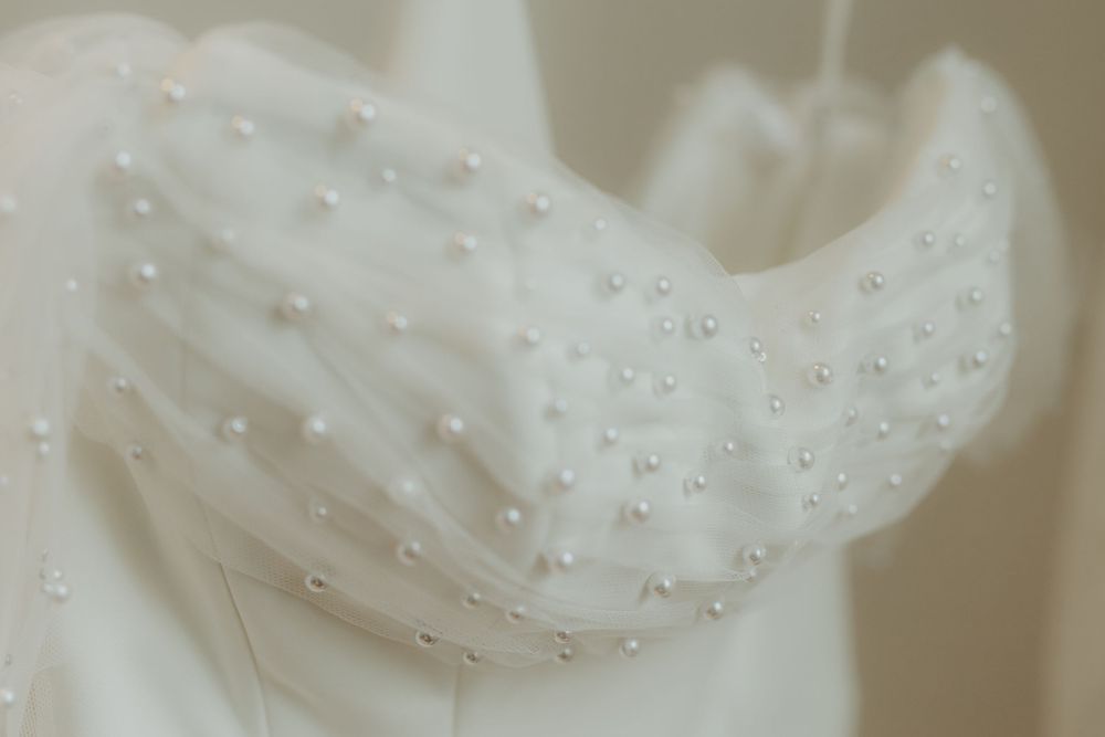Close-up of a white wedding dress bodice adorned with delicate pearl beading and sheer fabric detailing.