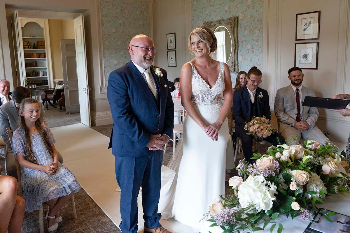 Bride and groom standing together during their wedding ceremony at the Belsfield Hotel, with guests seated nearby.