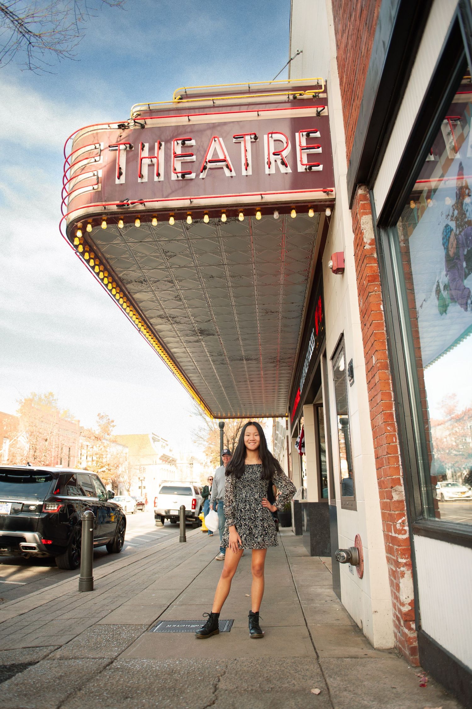 Young woman in floral dress and boots standing under a lit Franklin Theatre marquee sign on a city sidewalk.