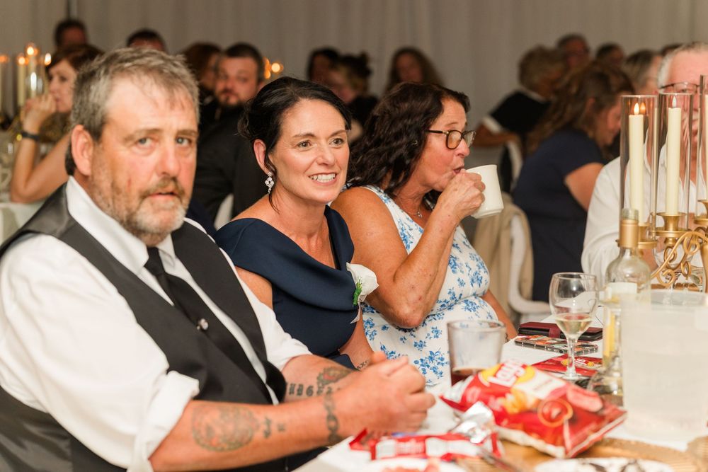 Guests smiling and laughing at a wedding reception dinner, seated at a decorated table in an elegant venue.