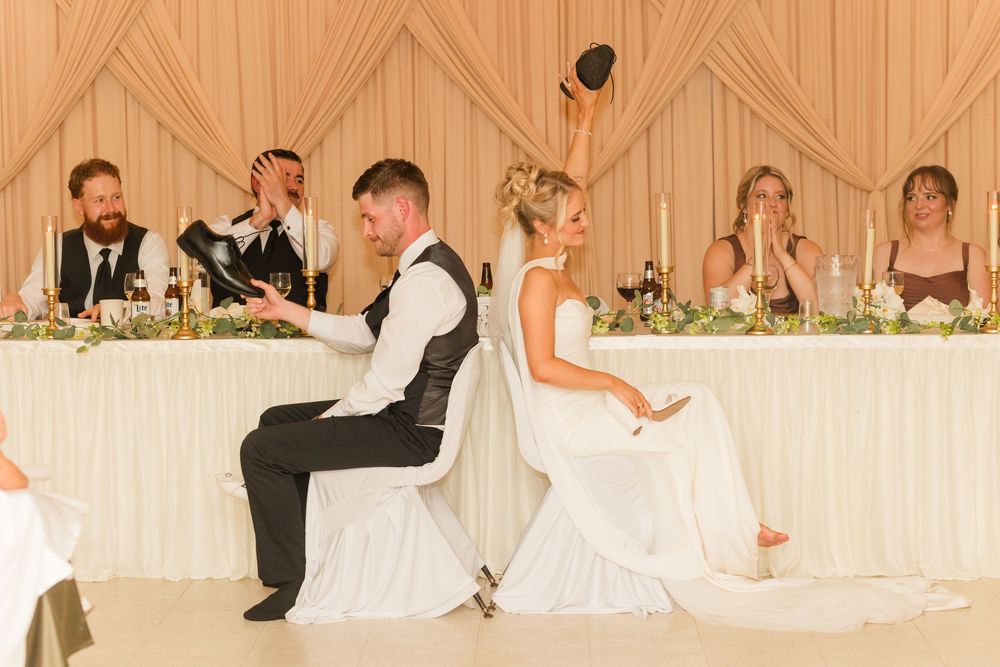 Bride and groom sit back-to-back playing a wedding shoe game at their elegant reception venue.