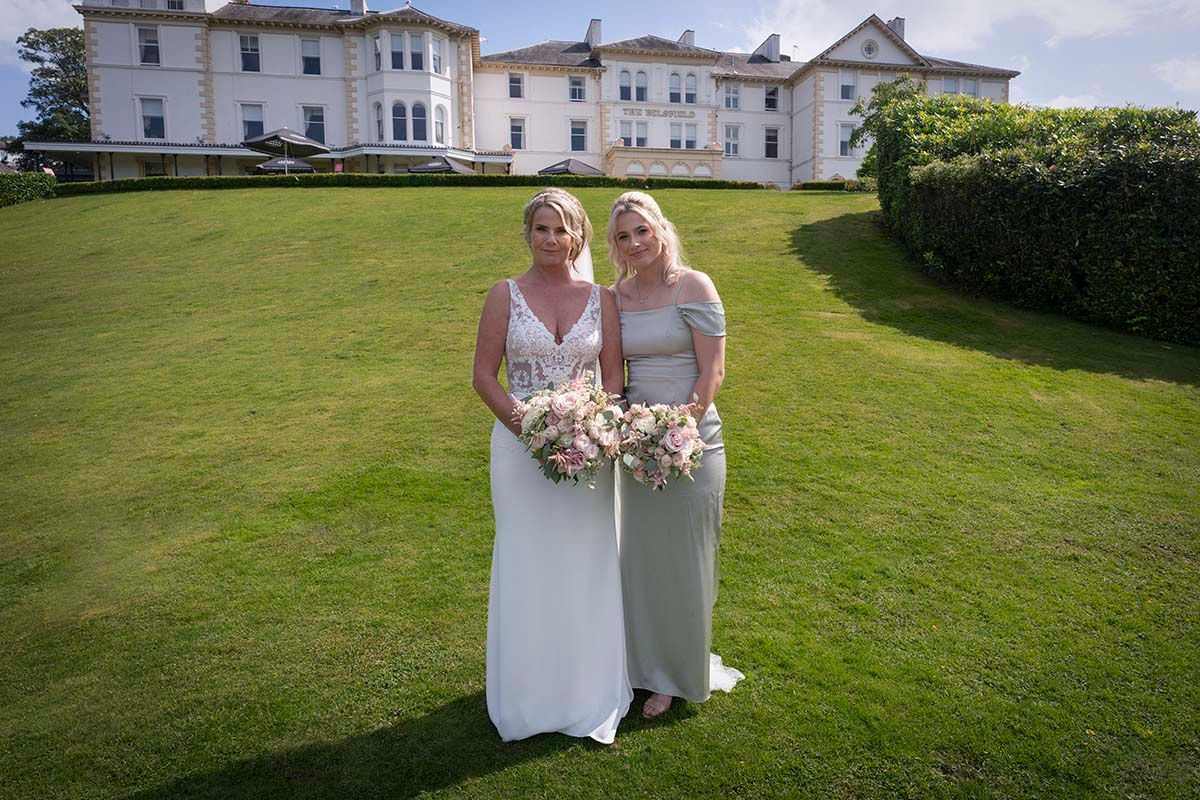Bride holding her bouquet beside her daughter on the lawn outside the Belsfield Hotel.