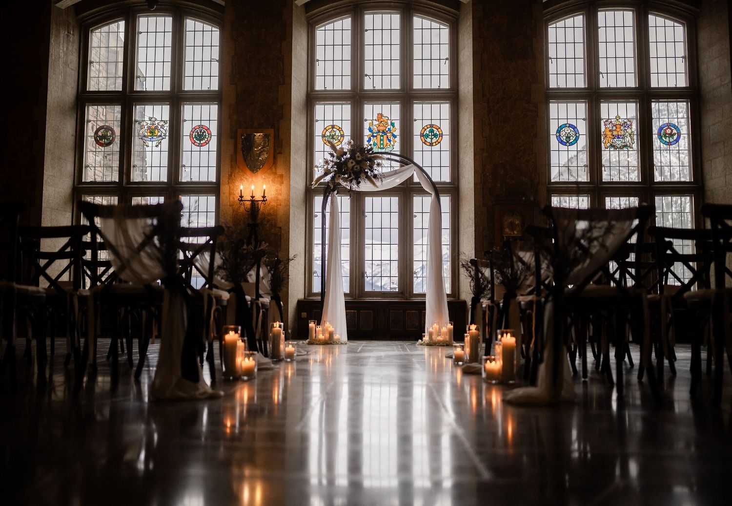 Candlelit aisle and white draped arch before stained-glass windows at a Fairmont Banff Springs Christmas wedding