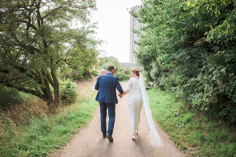 Brudepar går hen ad en sti mellem træer – bryllupsfoto af Martin & Louise