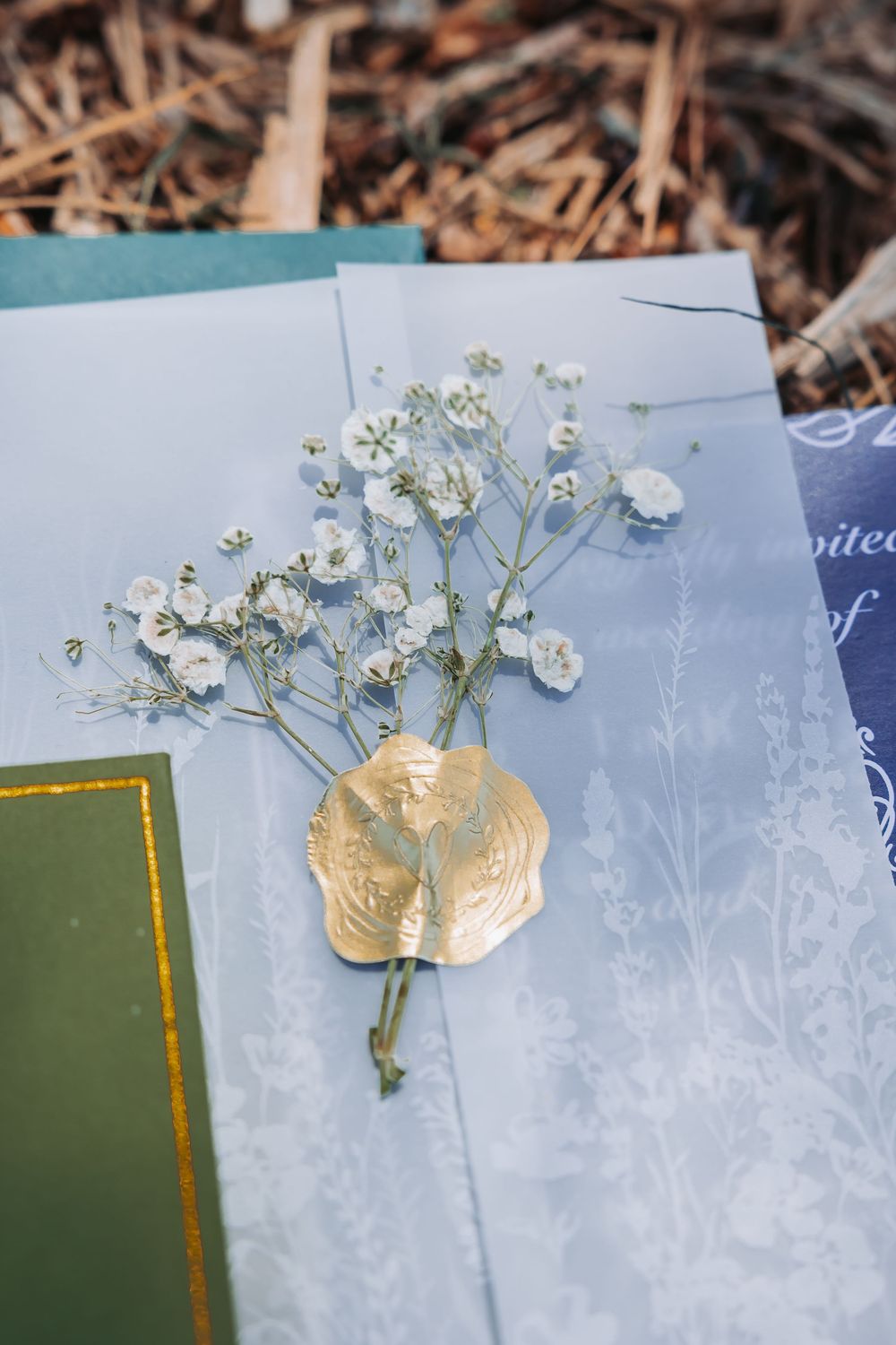 Gold wax seal with delicate white baby's breath flowers on elegant blue-gray vellum wedding invitation stationery.