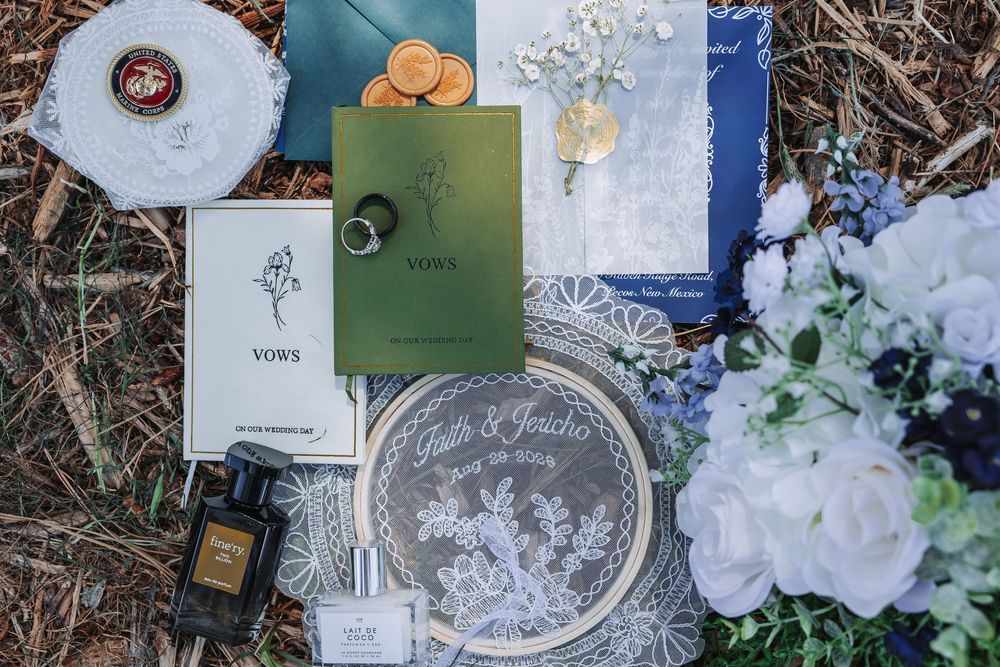 Elegant wedding flat lay with vow books, navy blue invitations, floral arrangements, and decorative stationery on a rustic background.