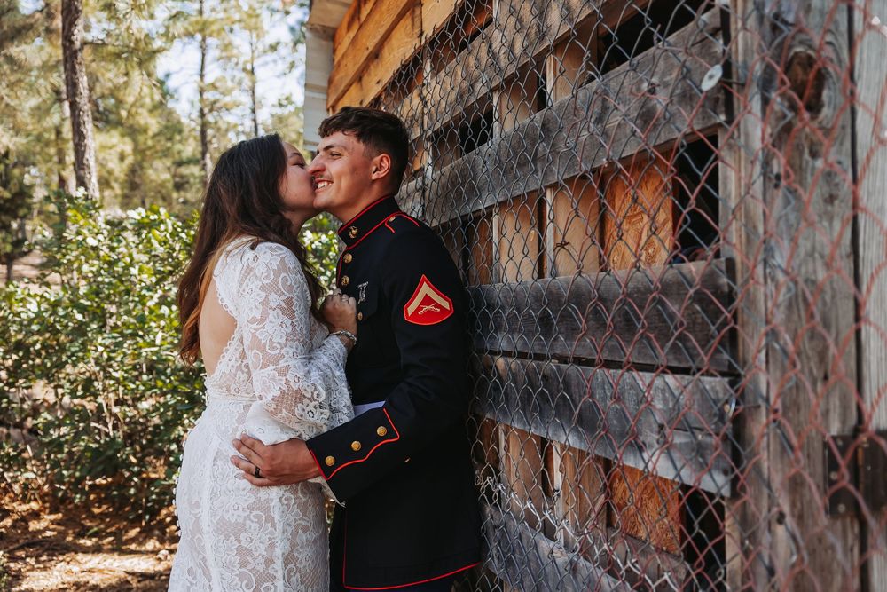 A Marine in dress uniform shares a romantic kiss with his bride in a lace wedding gown outdoors.