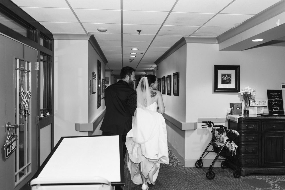Black and white photo of a bride and groom walking down a hallway on their wedding day.