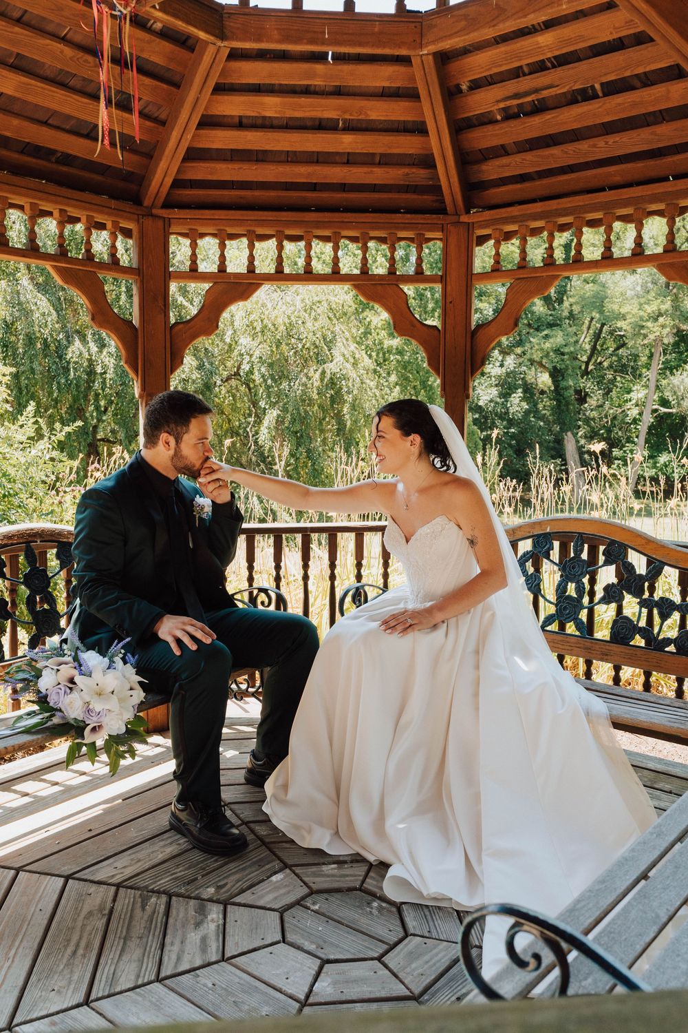 Bride and groom sit together in a wooden gazebo, sharing a tender moment surrounded by lush greenery.