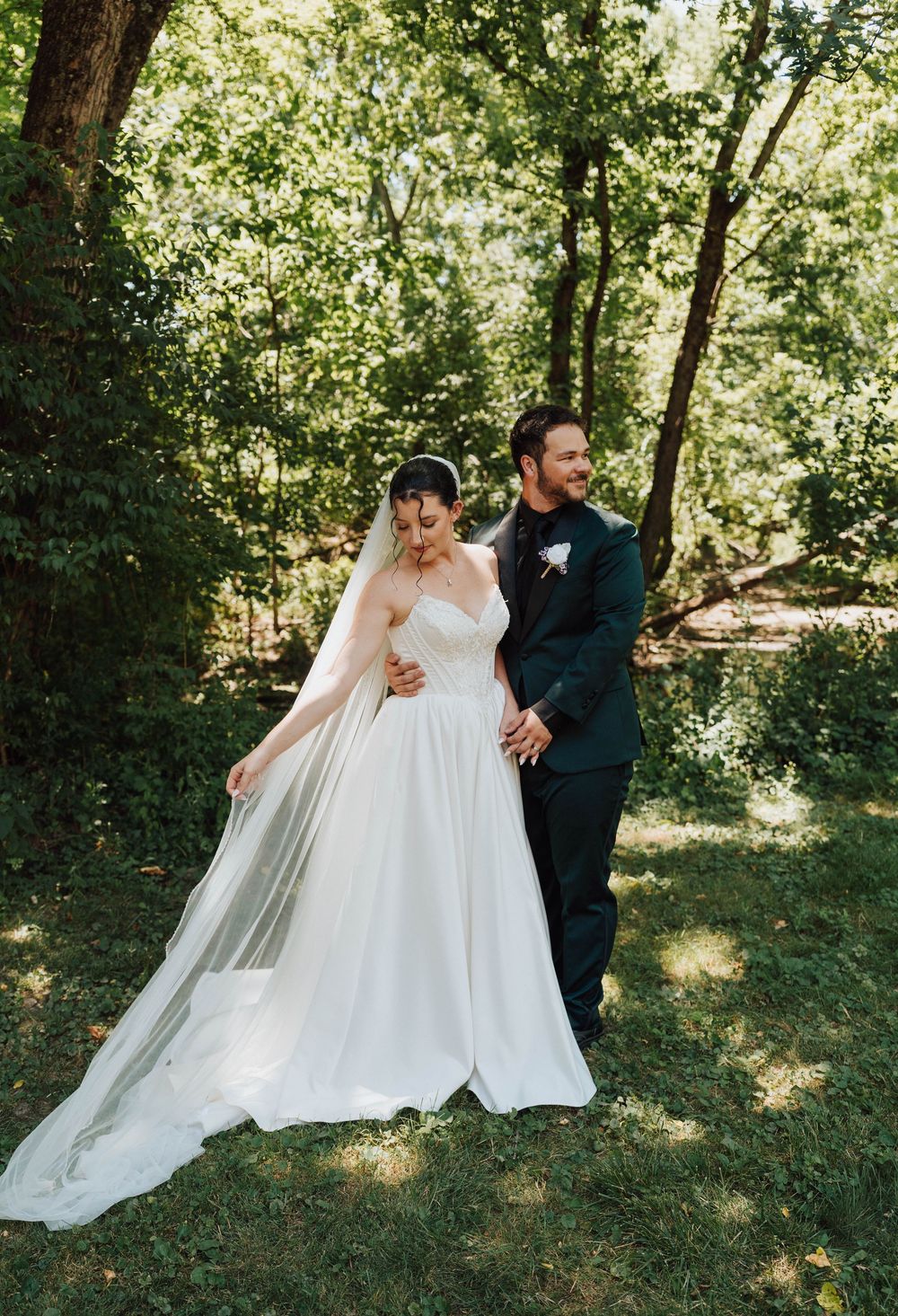 Bride and groom walking hand in hand through lush green forest, bride wearing elegant white ball gown with flowing veil.