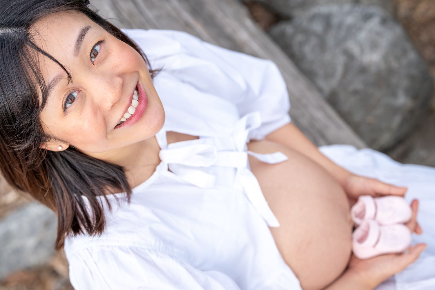 Smiling expectant mother holding a pair of baby shoes against her belly.