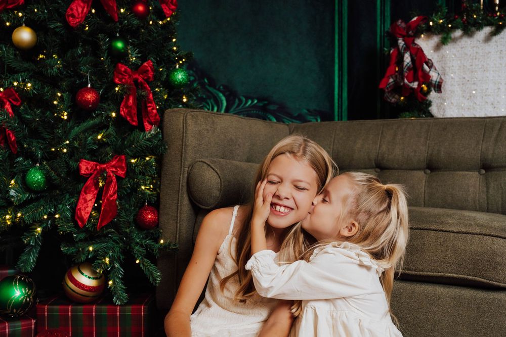 Two sisters seated together in front of a Christmas tree for Christmas mini sessions in Nicolle Aponte Photography's Middletown, PA studio.