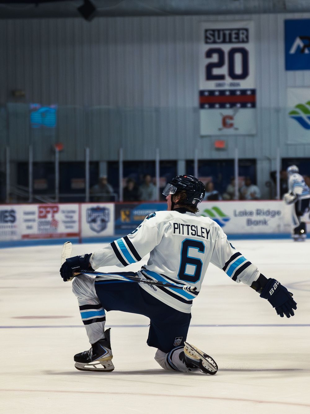 A Madison Capitols player number 6 drops to one knee with both arms spread wide in a goal celebration, seen from behind on the ice.