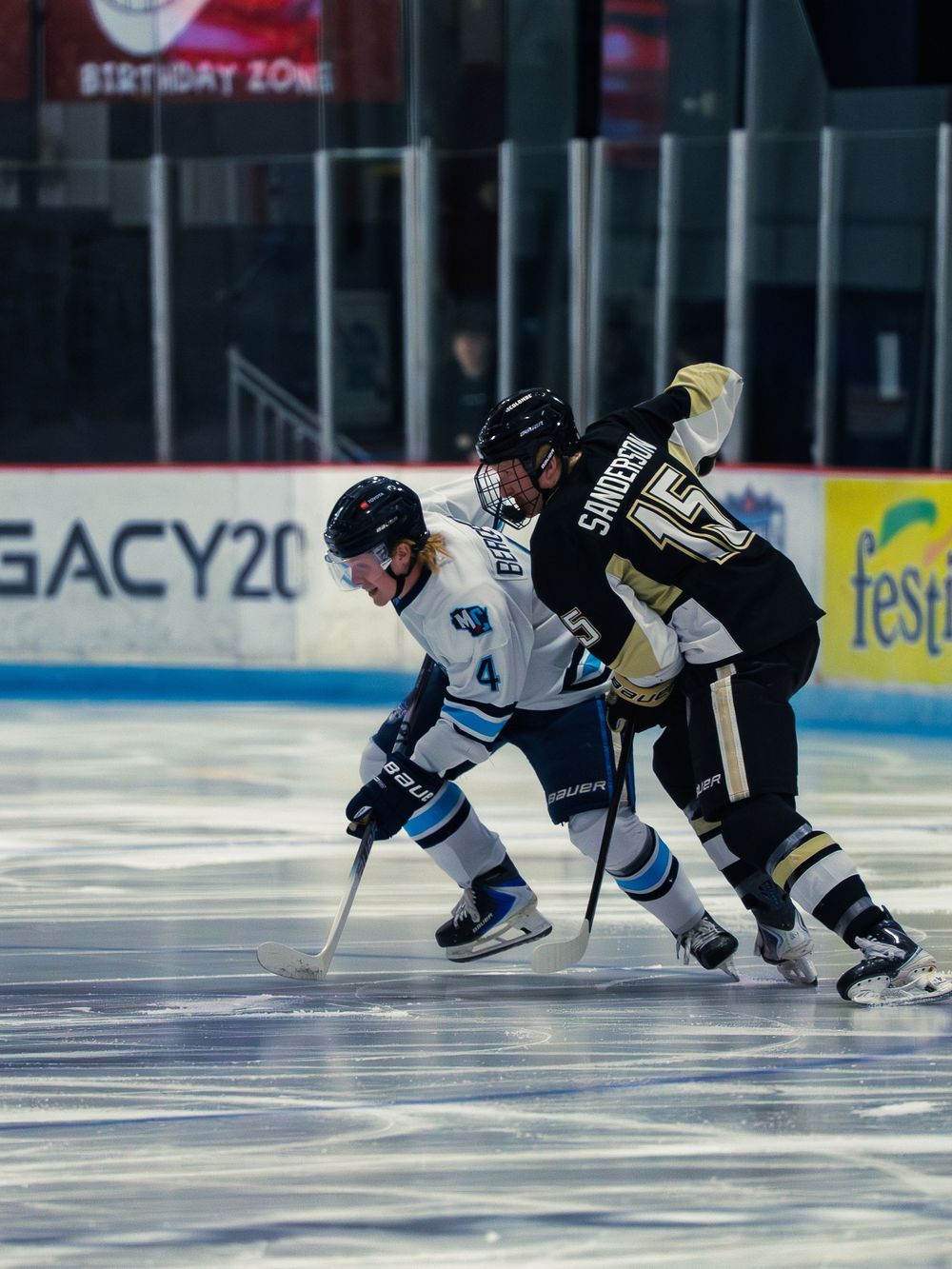 A Madison Capitols player number 4 leans shoulder-to-shoulder into a black-and-gold Lumberjacks player number 15 battling for the puck.