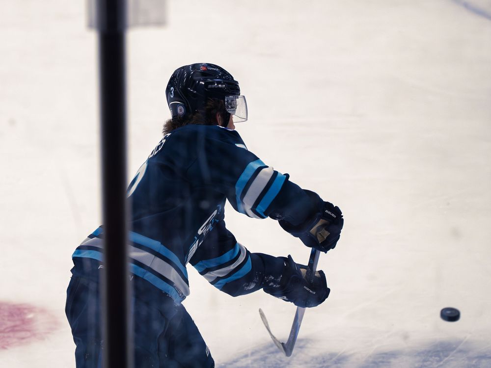 A Madison Capitols player number 3 follows through on a pass, seen from behind through the glass, the puck sliding away to his right.
