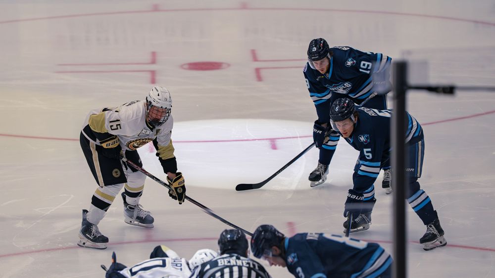 Madison Capitols and white-and-gold Lumberjacks players line up around the faceoff circle as a linesman prepares to drop the puck.