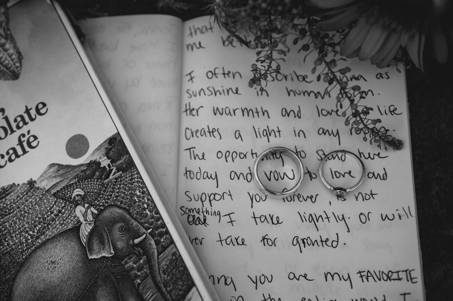 Black and white photo of an open journal with handwritten wedding vows next to a book with elephant illustration.