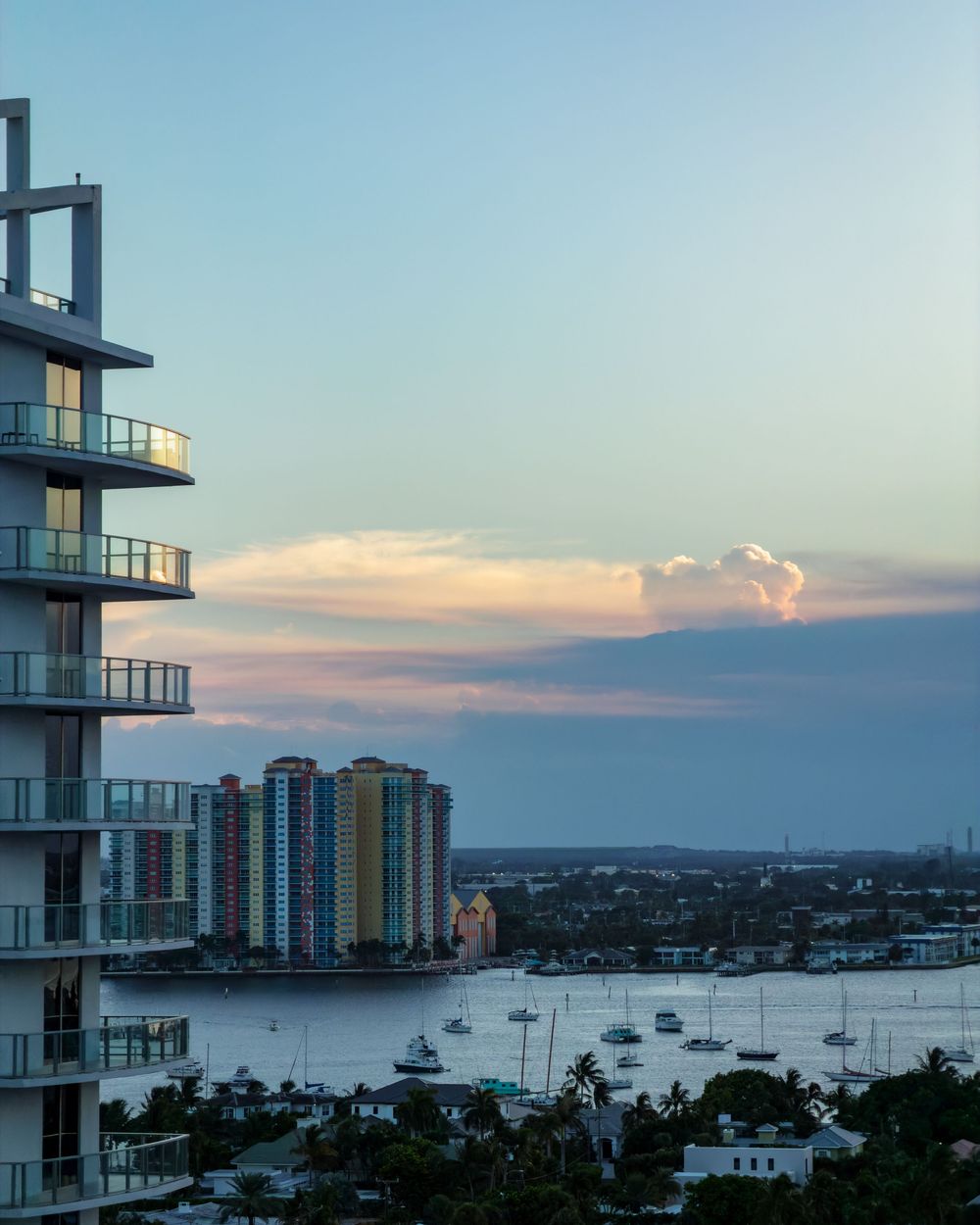Aerial dusk view of a modern high-rise building overlooking a colorful waterfront cityscape.