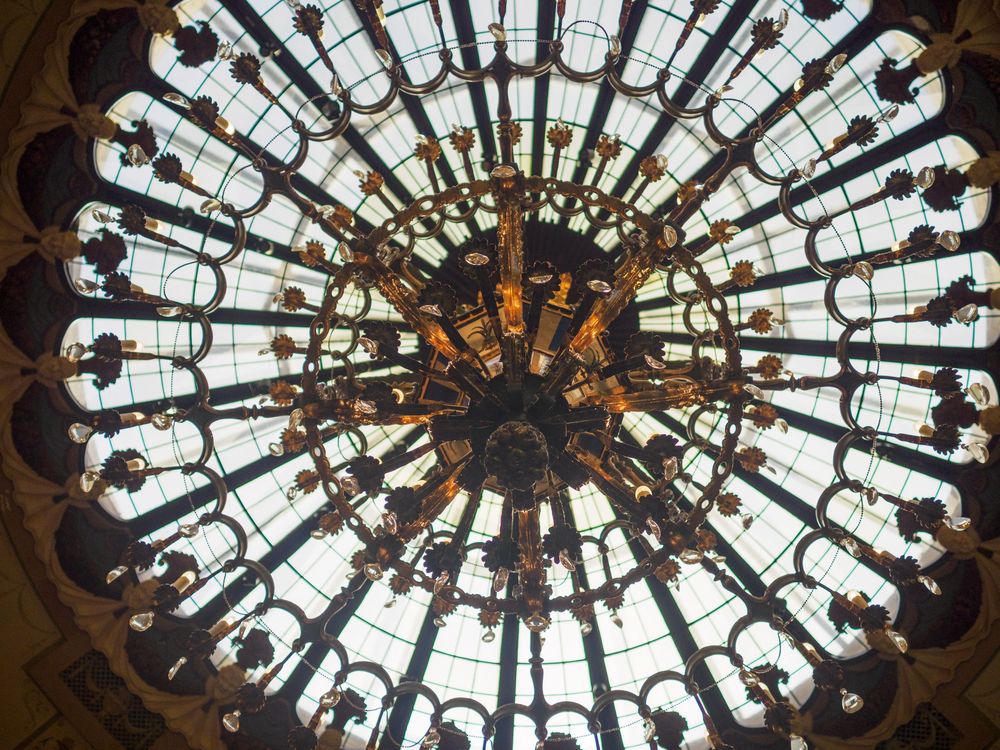 Stunning circular stained glass dome ceiling with ornate ironwork and central chandelier viewed from below.